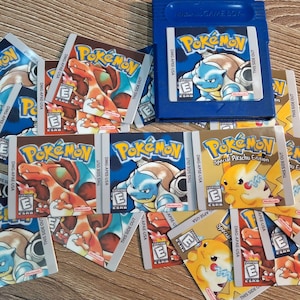 May include: A collection of 13 Pokemon game cartridge labels, featuring various Pokemon characters, including Pikachu, Squirtle, and Charizard. The labels are in different colors, including gold, blue, and red. The labels are for the Game Boy Color and Game Boy Advance.