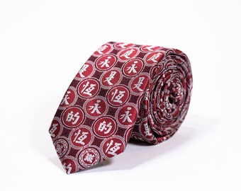 May include: A red silk tie with a white pattern of Chinese characters. The tie is rolled up and the pattern is visible on the outside of the roll.