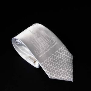 May include: A white silk tie with a gray honeycomb pattern and a white outline of the Salt Lake City Temple with the text "Salt Lake City Temple".
