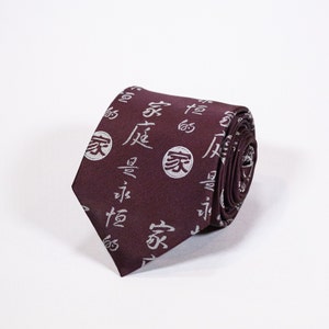 May include: A maroon silk tie with a white pattern of Chinese characters and circles. The tie is rolled up and the pattern is visible on the front and back.