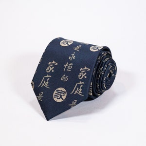 May include: A dark blue silk tie with a repeating pattern of gold Chinese characters and symbols. The tie is rolled up and the pattern is visible on the rolled portion.