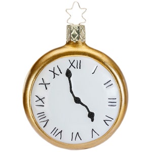 Puede incluir: Adorno navideño dorado con forma de reloj de bolsillo. La esfera blanca presenta números romanos negros y manecillas negras. Una estrella plateada remata el adorno.