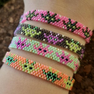 May include: Close-up of five beaded bracelets in various colours, including pink, brown, green, and orange. Each bracelet features a floral pattern. The bracelets are made of small, colourful beads.