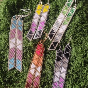 May include: Six pairs of beaded earrings in various colors, including blue, pink, yellow, green, and black. The earrings are rectangular with a feather-like design. They are displayed on a bed of green moss.