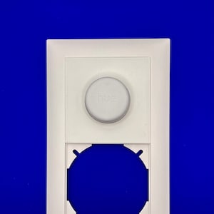 Könnte beinhalten: Weiße Kunststoff-Wandplatte mit einem runden Ausschnitt und einem weißen Knopf mit der Aufschrift "hue".