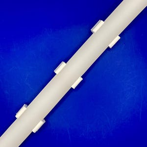 Peut inclure: Un objet cylindrique blanc avec plusieurs petites attaches rectangulaires blanches. L'objet est positionné en diagonale sur un fond bleu uni. Les attaches semblent espacées uniformément le long du cylindre.