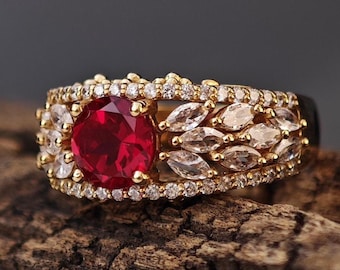 Puede incluir: Un anillo de oro con una gran piedra roja rodeada de piedras pequeñas transparentes.