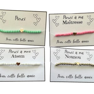 Könnte beinhalten: Vier Armbänder aus grünen, rosa, weißen und goldenen Perlen, jedes mit einem goldenen Herzanhänger. Die Armbänder werden auf Karten mit französischem Text und Herzillustrationen präsentiert. Auf den Karten steht "Merci" und "Pour cette belle année".
