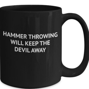 May include: Black coffee mug with white text that reads "HAMMER THROWING WILL KEEP THE DEVIL AWAY"