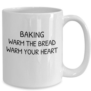 May include: White ceramic coffee mug with black text that reads "Baking warm the bread warm your heart".