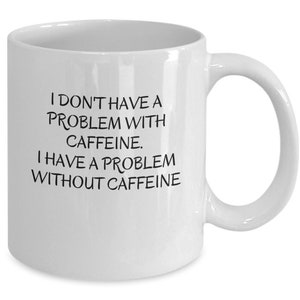 May include: White ceramic coffee mug with black text that reads "I don't have a problem with caffeine. I have a problem without caffeine."