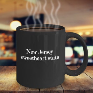 May include: Black coffee mug with white text that reads "New Jersey sweetheart state".