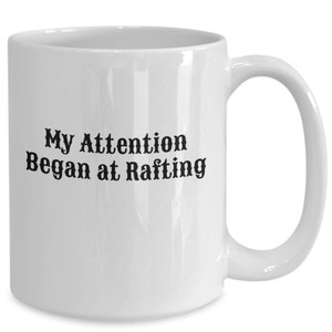 May include: White ceramic coffee mug with black text that reads "My Attention Began at Rafting".