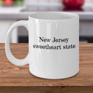May include: White ceramic coffee mug with a black inscription that reads "New Jersey sweetheart state".