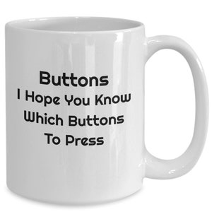 May include: White ceramic coffee mug with black text that reads "Buttons I Hope You Know Which Buttons To Press".
