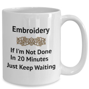 May include: White ceramic coffee mug with black text that reads "Embroidery If I'm Not Done In 20 Minutes Just Keep Waiting". A gold decorative design is above the text.