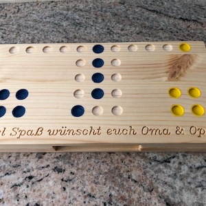 May include: A wooden game board with a message engraved on the bottom: "Viel Spaß wünscht euch Oma & Opa". The board has 24 holes and is filled with blue and yellow game pieces.