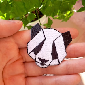 Può includere: Una toppa ricamata a forma di panda, in bianco e nero. Il panda ha un design semplice con occhi neri e un naso nero.