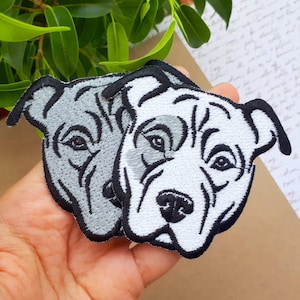 May include: Two embroidered iron-on patches of pit bull dogs. One patch is grey and the other is white.