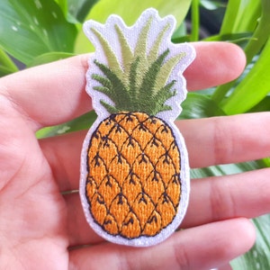 May include: Embroidered pineapple patch with a white background, green leaves, and a yellow pineapple with brown details.