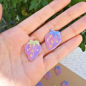 Puede incluir: Dos parches bordados para planchar de fresas rosas con semillas amarillas y hojas verdes. Las fresas tienen un efecto degradado morado.