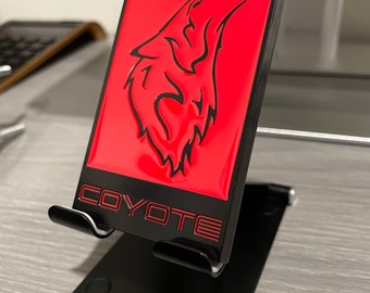 May include: A black metal phone stand with a red metal plate featuring a black silhouette of a howling wolf and the word "COYOTE" in black lettering.