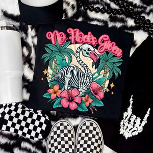 Puede incluir: Camiseta negra con un gráfico de flamenco esquelético y el texto "No F*cks Given". El flamenco está rodeado de plantas y flores tropicales.