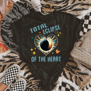May include: Black t-shirt featuring a graphic of a heart-shaped eclipse with the text "TOTAL ECLIPSE OF THE HEART".