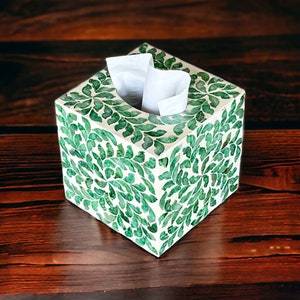 May include: A white tissue box cover with a green floral design. The cover is made of a material that looks like mother of pearl.