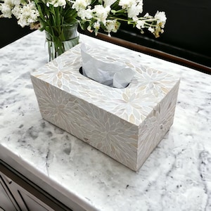 May include: A white tissue box cover with a floral pattern made of mother of pearl. The cover is sitting on a white marble surface.