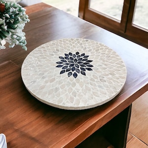 Può includere: Un vassoio rotondo in mosaico bianco e nero con un motivo floreale. Il vassoio è fatto di madreperla e ha un centro nero.