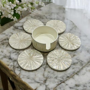 Può includere: Set di sei sottobicchieri in madreperla bianca con un porta-sottobicchieri abbinato. I sottobicchieri hanno un design a raggiera.