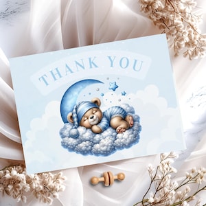 May include: Blue thank you card with a cartoon illustration of a teddy bear sleeping on a cloud with a crescent moon and stars. The text "THANK YOU" is printed in a light blue font.