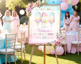 May include: A wooden easel displays a baby shower sign with popsicle graphics and the text "SHE'S READY TO POP." The sign welcomes guests to "Valencia's BABY SHOWER!" on August 30th, 2-6 PM. Floral arrangements and balloons decorate the outdoor event.