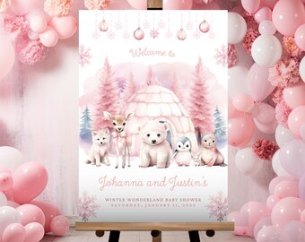 May include: A baby shower sign on an easel with a winter wonderland theme. The sign features illustrations of arctic animals, an igloo, and pine trees in shades of pink and white. The text reads "Welcome to Johanna and Justin's Winter Wonderland Baby Shower Saturday, January 11, 2025."