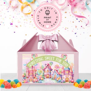 Può includere: Una scatola a gabbia rosa con un fiocco rosa in cima. La scatola ha un'etichetta con un'illustrazione colorata di una città di caramelle e il testo "Something Sweet For You!"