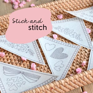 May include: A set of five white triangle-shaped fabric panels with gray embroidery designs. The panels are pinned to a woven basket with pink pins. The text "Stick and stitch" is written on a pink background.