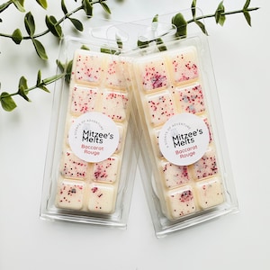 May include: Two packs of wax melts in clear plastic packaging. Each pack contains six square wax melts with a white base and red glitter. The label on each pack reads "A Scents of Adventure Mitzee's Melts Baccarat Rouge".
