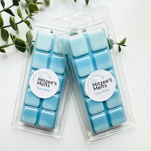 May include: Two packs of blue wax melts in clear plastic packaging. Each pack has six squares of wax melt and a round label that says "Scents of Adventure Mitzee's Melts The Male".
