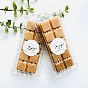 May include: Two clear plastic clamshell packages containing tan wax melts. Each package features a round white label with the text Mitzee's Melts Nag Champa and a small icon. The wax cubes are light brown with scattered copper-coloured glitter.