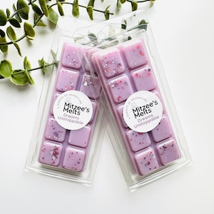 May include: Two clear plastic clamshell packages containing light purple wax melts with embedded pink, silver, and purple glitter. Each package features a circular white label with the text Mitzee's Melts and Dreams Unstoppable.