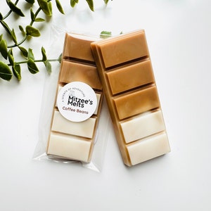 May include: Two coffee bean-scented wax melt bars. One bar is in a clear plastic package with a white label that reads "Mitzee's Melts Coffee Beans." The other bar is next to the packaged bar. The bars are a gradient of white, tan, and brown.