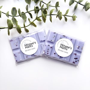 May include: Two rectangular light purple wax melts in clear plastic packaging. Each bar features a circular white label with the text Mitzee's Melts Stress Less and a small icon. The wax is embedded with small, reflective purple and silver glitter.