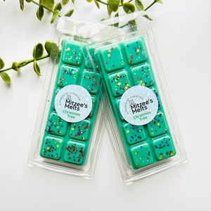 May include: Two packs of teal wax melts with a Christmas tree scent. The wax melts are in clear plastic packaging and have a white label with the text "A Scents of Christmas, Mitzee's Melts, Christmas Tree".