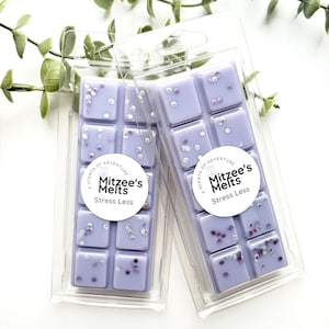 May include: Two lavender wax melt bars in clear plastic packaging. Each bar is divided into six squares and decorated with small, white and purple sprinkles. The packaging includes a round label that reads "Mitzee's Melts Stress Less."