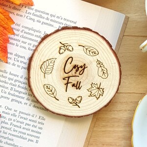 Peut inclure: Un dessous de verre en bois avec un motif gravé de feuilles et de glands. Le texte "Cozy Fall" est au centre du dessous de verre.