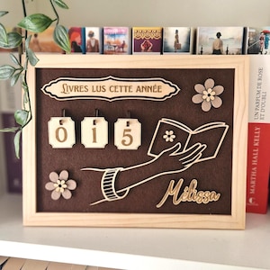 Op de afbeelding: Houten boektracker met de tekst "Livres Lus Cette Année" en het nummer "015". Het ontwerp bevat een hand die een boek vasthoudt en de naam "Melissa". Decoratieve houten bloemen zijn ook inbegrepen.