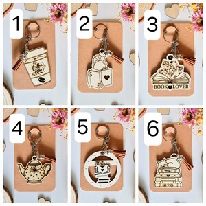 Peut inclure: Six différents porte-clés en bois avec un fond brun. Les porte-clés représentent une tasse de café, une femme lisant un livre, un livre avec le texte "BOOK LOVER", une théière, une pile de livres avec le nom "Melissa" et un chat dormant sur une pile de livres.