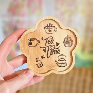 Peut inclure: Un dessous de verre en bois en forme de fleur avec un motif de l'heure du thé. Le dessous de verre représente une tasse à thé, une théière, un sachet de thé et un cupcake.