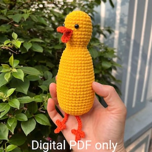 May include: A crocheted yellow chick toy with orange feet and beak. The chick is being held in a hand.